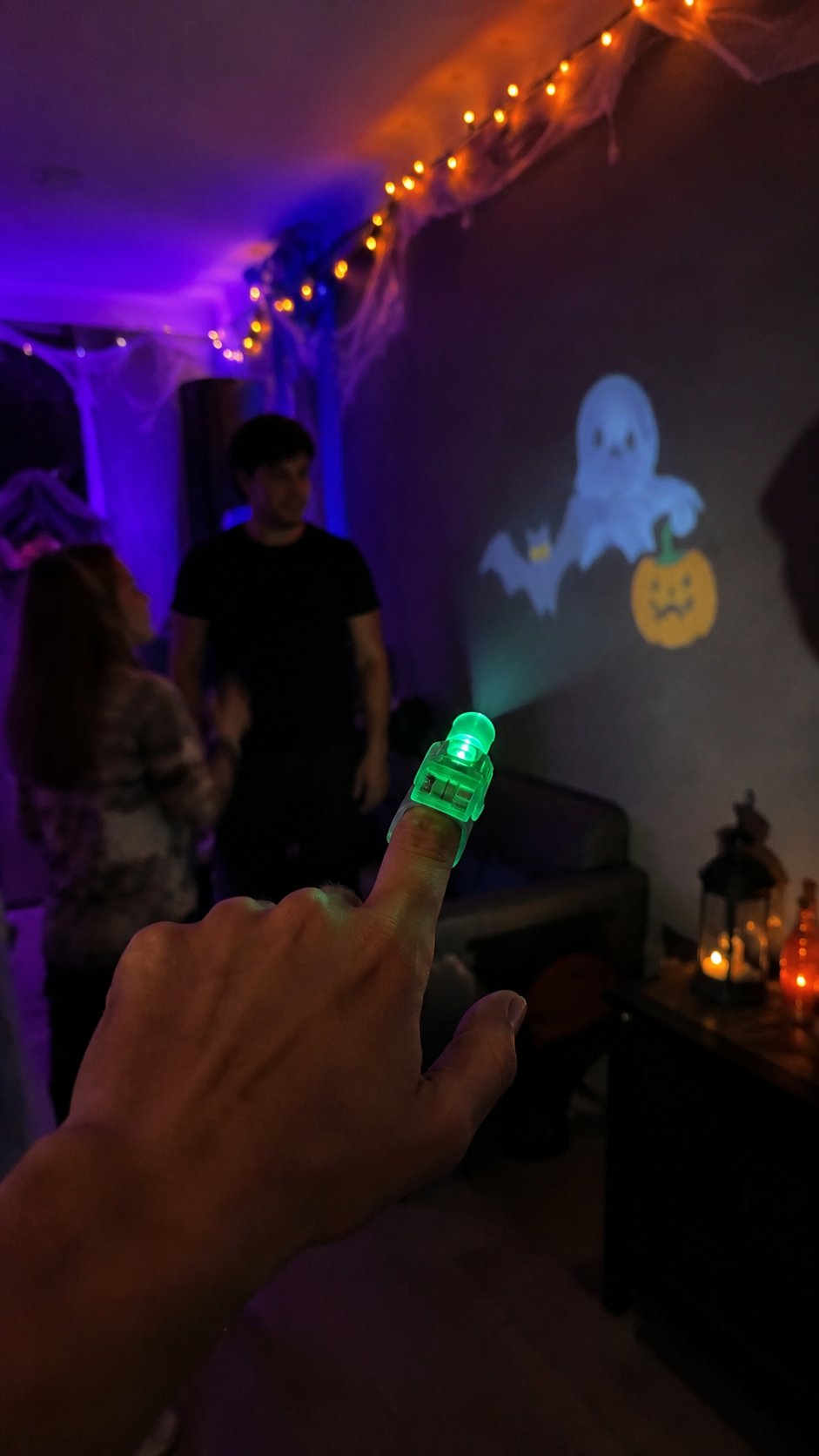 Vertical Halloween party lifestyle photo showing a green finger projector and projected ghost and pumpkin patterns